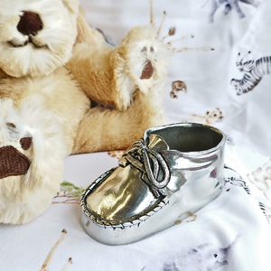 Pewter metal baby boot sitting next to a teddy bear and on a blanket