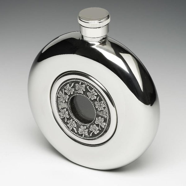 WHISKEY FLASK WITH GLASS CENTRE AND SHAMROCK DESIGN. THE FLASK IS 4" TALL AND HOLDS 5 FLUID OZS. THE DECORATIVE GLASS CENTER IS SURROUNDED BY TRELLIS SHAMROCK PEWTER DESIGN. MADE IN IRELAND BY MULLINGAR PEWTER.