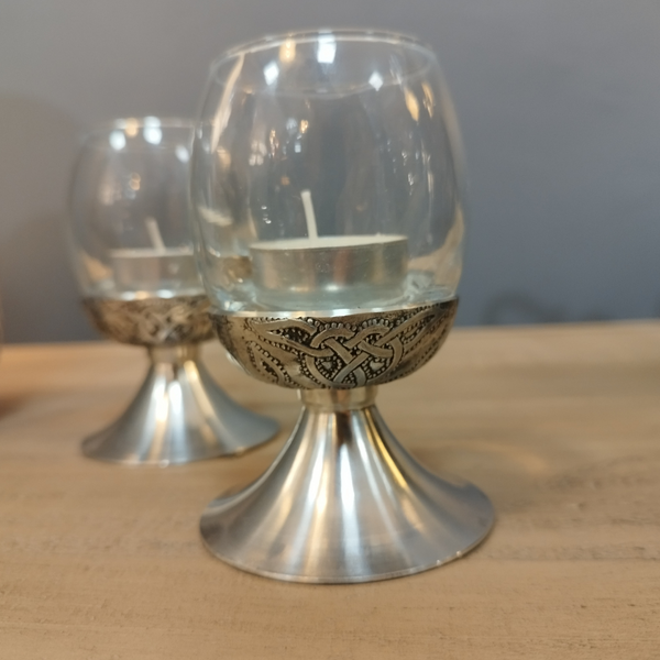 A Celtic knotwork design tea light holder made of pewter with a glass insert, displaying a candle.