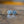 Load image into Gallery viewer, A pair of round silver-toned tie pins with a textured border and a central raised emblem, resting on a wooden surface with a soft reflection.
