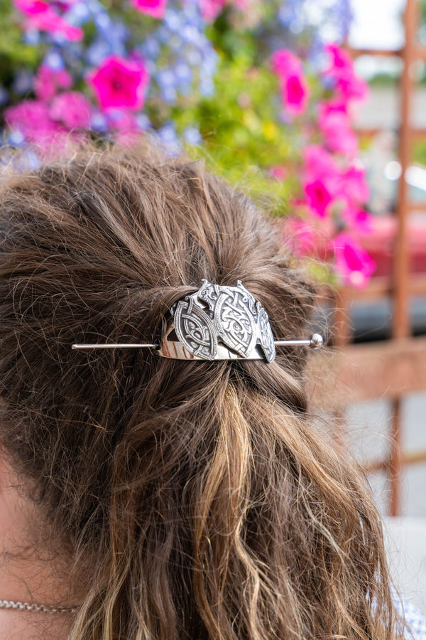 A close-up lifestyle shot of a person's brown hair tied back with a decorative silver-toned metal hair stick featuring an intricate Celtic knot pattern.