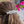 Load image into Gallery viewer, A close-up lifestyle shot of a person's brown hair tied back with a silver-toned, intricately woven hair accessory, set against a blurred background of colorful flowers.
