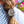 Load image into Gallery viewer, A close-up of a person's brown braided hair secured with a round, textured silver-toned hair tie, wearing a blue and white patterned top with a blurred garden background.
