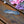 Load image into Gallery viewer, A silver-toned metal bar with an intricate Celtic knot pattern, resting on a rustic wooden surface with pink and purple flowers in the background.
