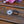 Load image into Gallery viewer, A silver-toned Celtic triquetra knot hair tie with a black elastic band, resting on a rustic wooden surface with pink and purple flowers in the background.
