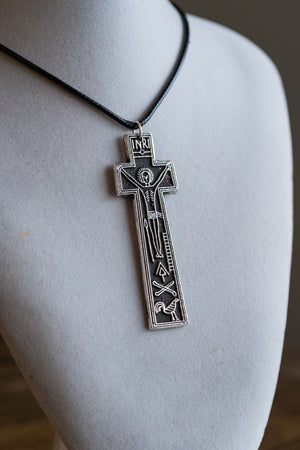 A silver-toned crucifix pendant necklace with an engraved figure of Jesus on a black cord, displayed on a light gray mannequin bust.
