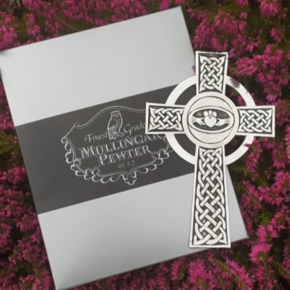 Mullingar Pewter Wall hanging cross with Celtic knot work and a Claddagh embellishment resting on a Mullingar Pewter presentation box and on a beautiful bed of pink heather