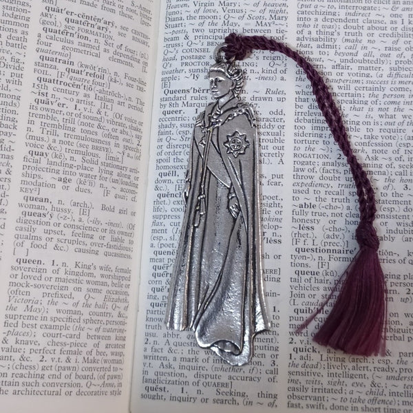 close up of the Queen Elizabeth Pewter Metal bookmark. It is resting on a dictionary. There is a maroon tassel on the bookmark