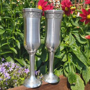 Beautiful handcrafted silver pewter drinking flutes with a celtic motif on the rim. A pair. resting among beautiful red flowers